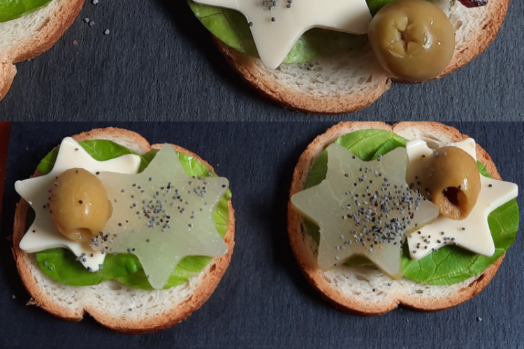 Trois bouchées festives présentées sur des tranches de pain, décorées de feuilles vertes, étoiles de fromage blanc et de betterave, olives vertes et graines de pavot. Chaque composition évoque une ambiance de fête, avec une touche créative et végétale. En bas, une bouchée repose sur une serviette en forme de sapin, renforçant l’esprit de Noël.