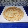 Une pile de crêpes fines et dorées, présentées sur une assiette carrée blanche, posée sur une nappe bleue éclatante. Les crêpes montrent une cuisson parfaite avec des motifs marbrés appétissants.