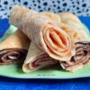 Assiette verte de crêpes express garnies de confiture et chocolat, posée sur une nappe bleue avec un fond à motifs noirs. Recette La Réunion des Cuisines.