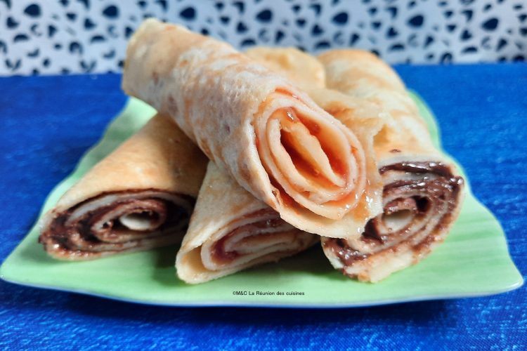 Assiette verte de crêpes express garnies de confiture et chocolat, posée sur une nappe bleue avec un fond à motifs noirs. Recette La Réunion des Cuisines.