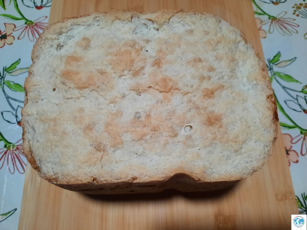 Une vue d'ensemble d'un pain maison rectangulaire, cuit en machine à pain et posé sur une planche à découper en bois. Sa mie est claire et sa croûte dorée est légèrement rustique.
