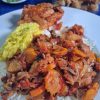Assiette de riz blanc garnie d'un rougail morue aux carottes fondant. À côté, un rougail mangue jaune vif et une pièce de poulet. En arrière-plan, un bol de rougail morue frite croustillante et une coupelle de piments frais