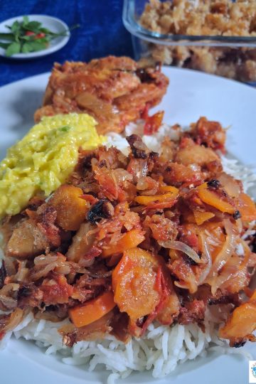 Assiette de riz blanc garnie d'un rougail morue aux carottes fondant. À côté, un rougail mangue jaune vif et une pièce de poulet. En arrière-plan, un bol de rougail morue frite croustillante et une coupelle de piments frais