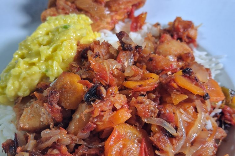 Assiette de riz blanc garnie d'un rougail morue aux carottes fondant. À côté, un rougail mangue jaune vif et une pièce de poulet. En arrière-plan, un bol de rougail morue frite croustillante et une coupelle de piments frais