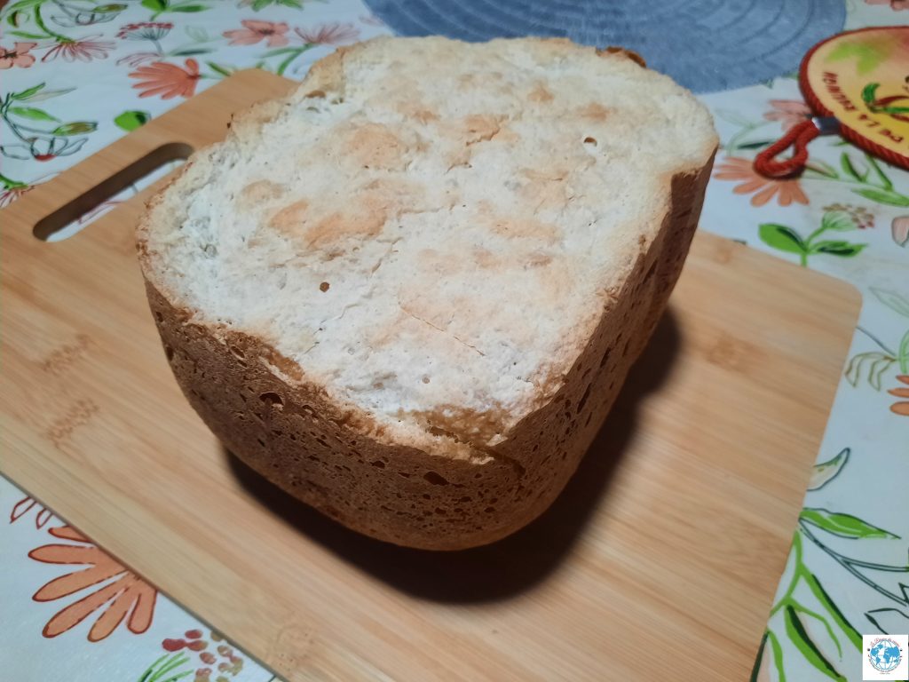 Vue de dessus d'un pain à la patate douce cuit en machine à pain, posé sur une planche à découper en bois. La croûte supérieure est claire avec des nuances dorées et présente une texture légèrement craquelée et rustique.