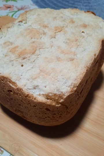 Vue de dessus d'un pain à la patate douce cuit en machine à pain, posé sur une planche à découper en bois. La croûte supérieure est claire avec des nuances dorées et présente une texture légèrement craquelée et rustique.
