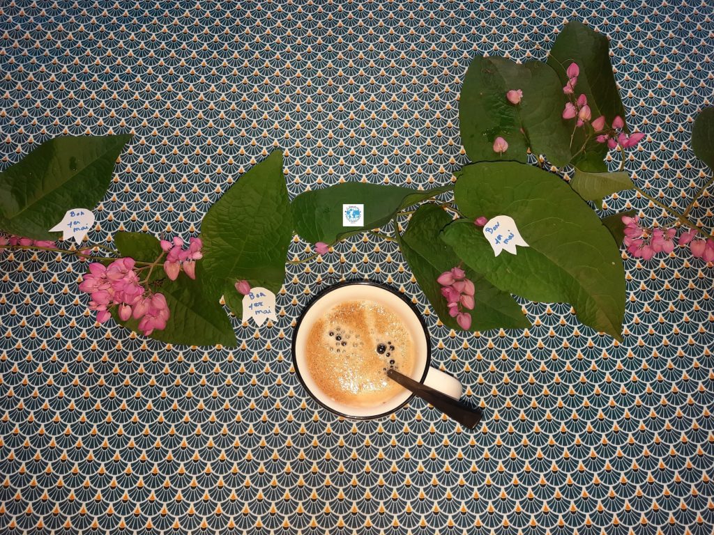 Déco de table 1er mai avec lianes de corail roses et tasse de café.