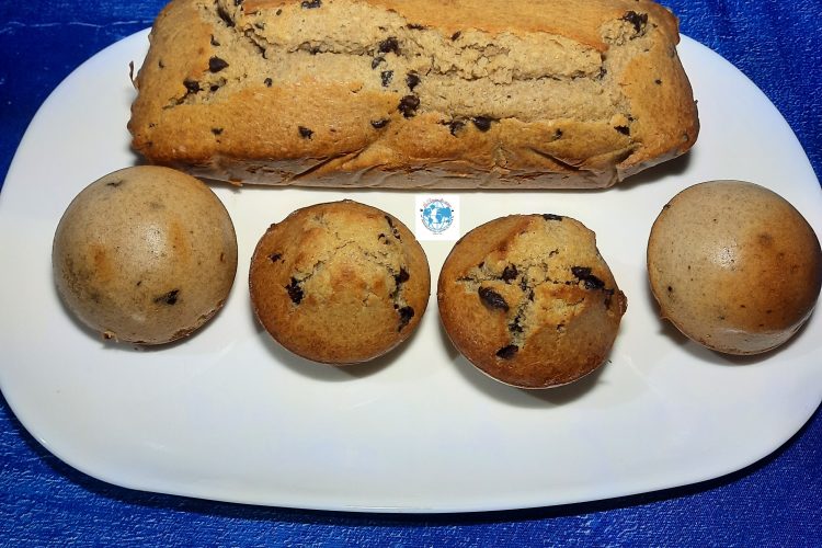 Gros plan en plongée d'une assiette ovale blanche remplie de pâtisseries maison dorées : un cake long aux pépites de chocolat et quatre petits gâteaux individuels, dont deux dômes retournés bombés et deux dômes lisses aux pépites. L'assiette est posée sur un fond bleu texturé.