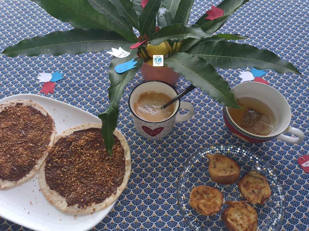 Petit-déjeuner gourmand du 1er mai comprenant des tortillas choco-pralin, du pain aux œufs frit, un café et une tisane péi, avec une décoration en feuilles de manguier.