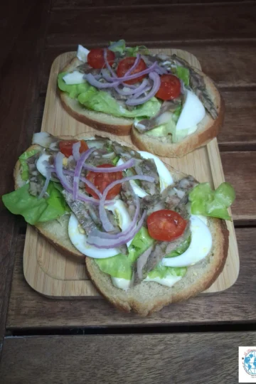 Délicieuses tartines créoles sur un plateau en bois, garnies de tomates cerises, oignons rouges, fromage de tête et œufs.