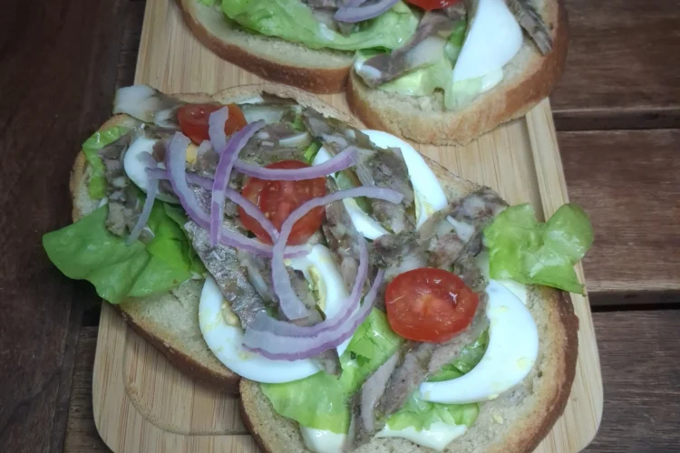 Délicieuses tartines créoles sur un plateau en bois, garnies de tomates cerises, oignons rouges, fromage de tête et œufs.