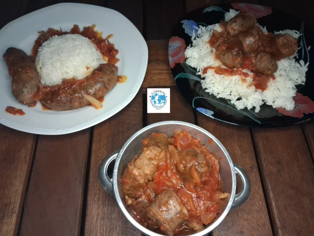Trois portions de rougail saucisse réunionnais aux tomates et oignons : deux assiettes dressées avec un dôme de riz blanc et une petite marmite en inox garnie au premier plan, le tout posé sur une table en bois sombre.