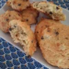 Une vue en plongée montre un plateau rectangulaire blanc garni de plusieurs biscuits dorés aux pépites de chocolat. Certains biscuits sont présentés entiers, tandis que d'autres sont disposés en deux morceaux, révélant une texture intérieure moelleuse et aérée. L'ensemble est posé sur une nappe ornée d'un motif géométrique répétitif en forme d'éventails bleu foncé et jaune sur fond bleu clair.